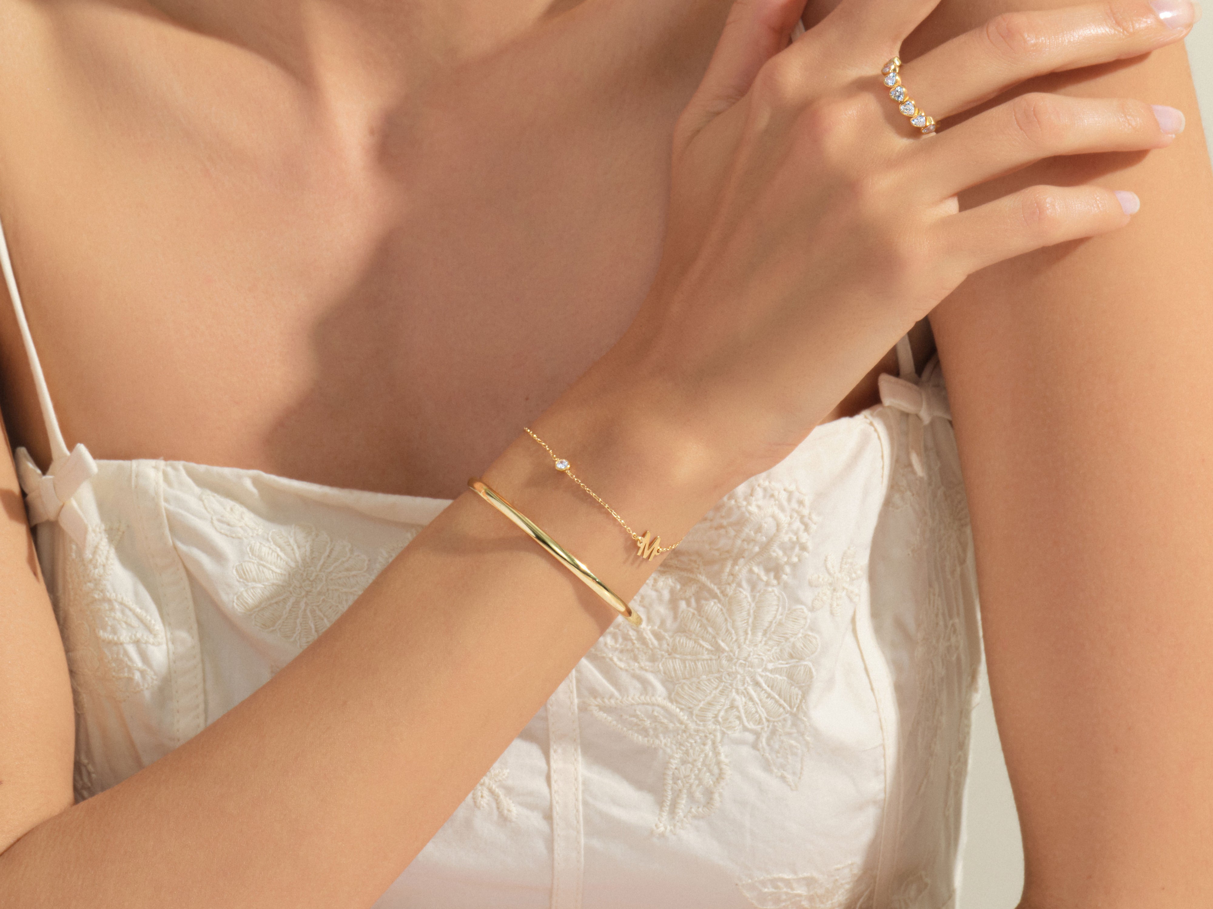 Gold bracelet with initial charm and diamond ring on hand