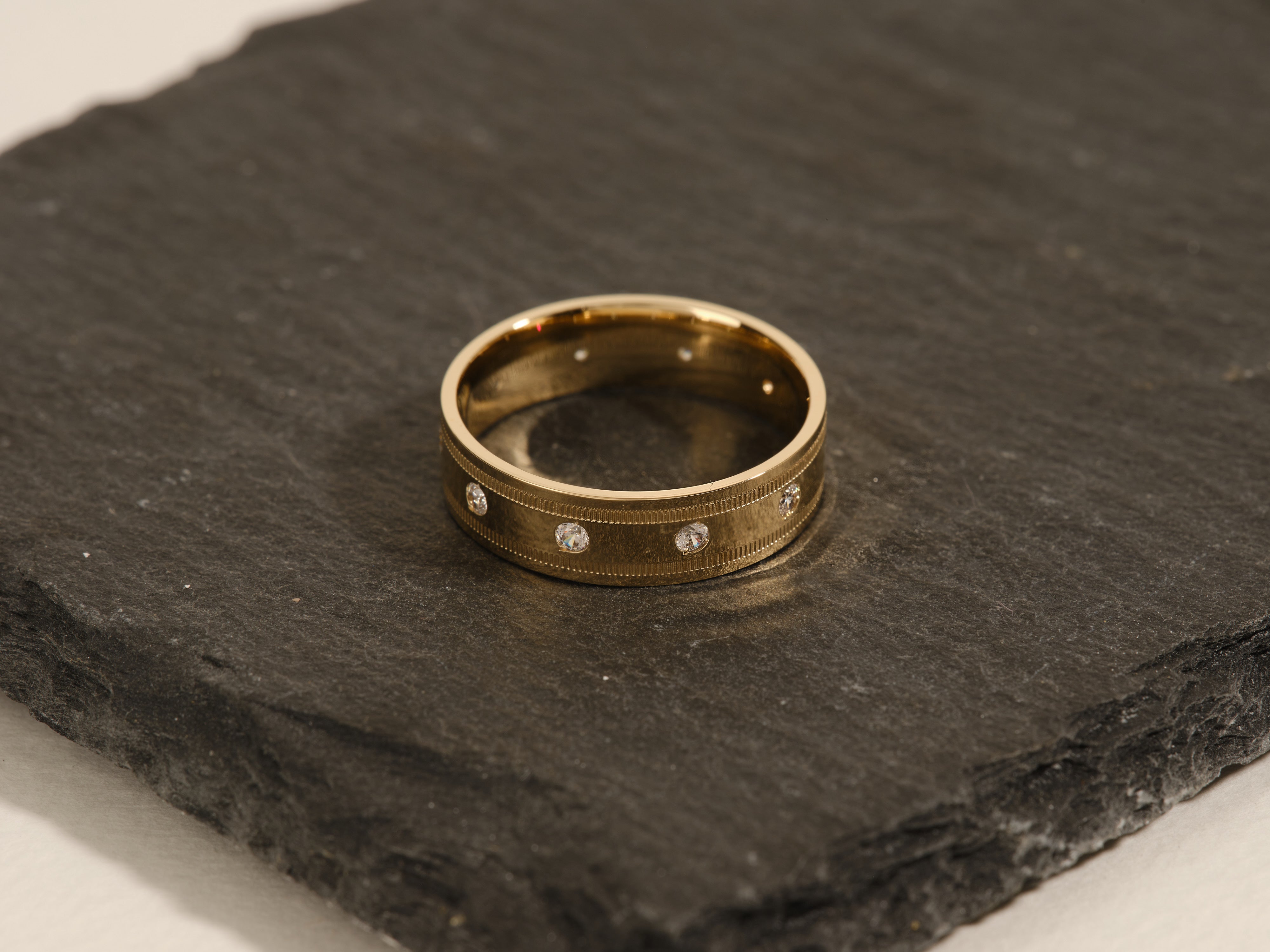 Gold band ring with diamonds on dark slate