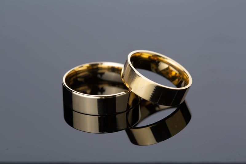 Two polished gold wedding bands on a reflective surface