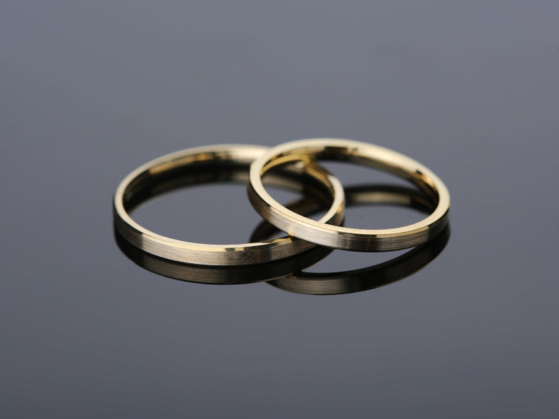 Two brushed gold wedding bands on reflective surface