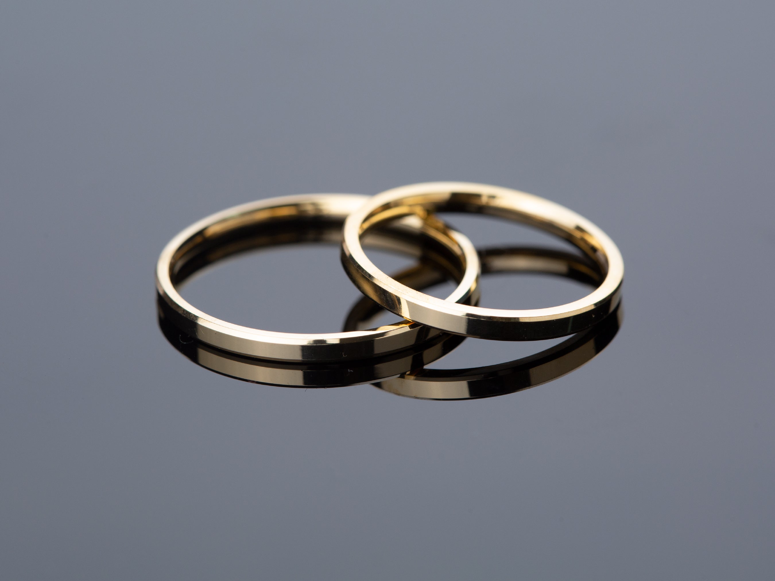 Two gold wedding bands on a reflective surface
