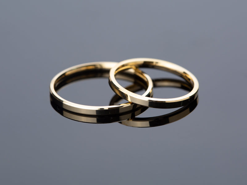 Two gold wedding bands on a reflective surface