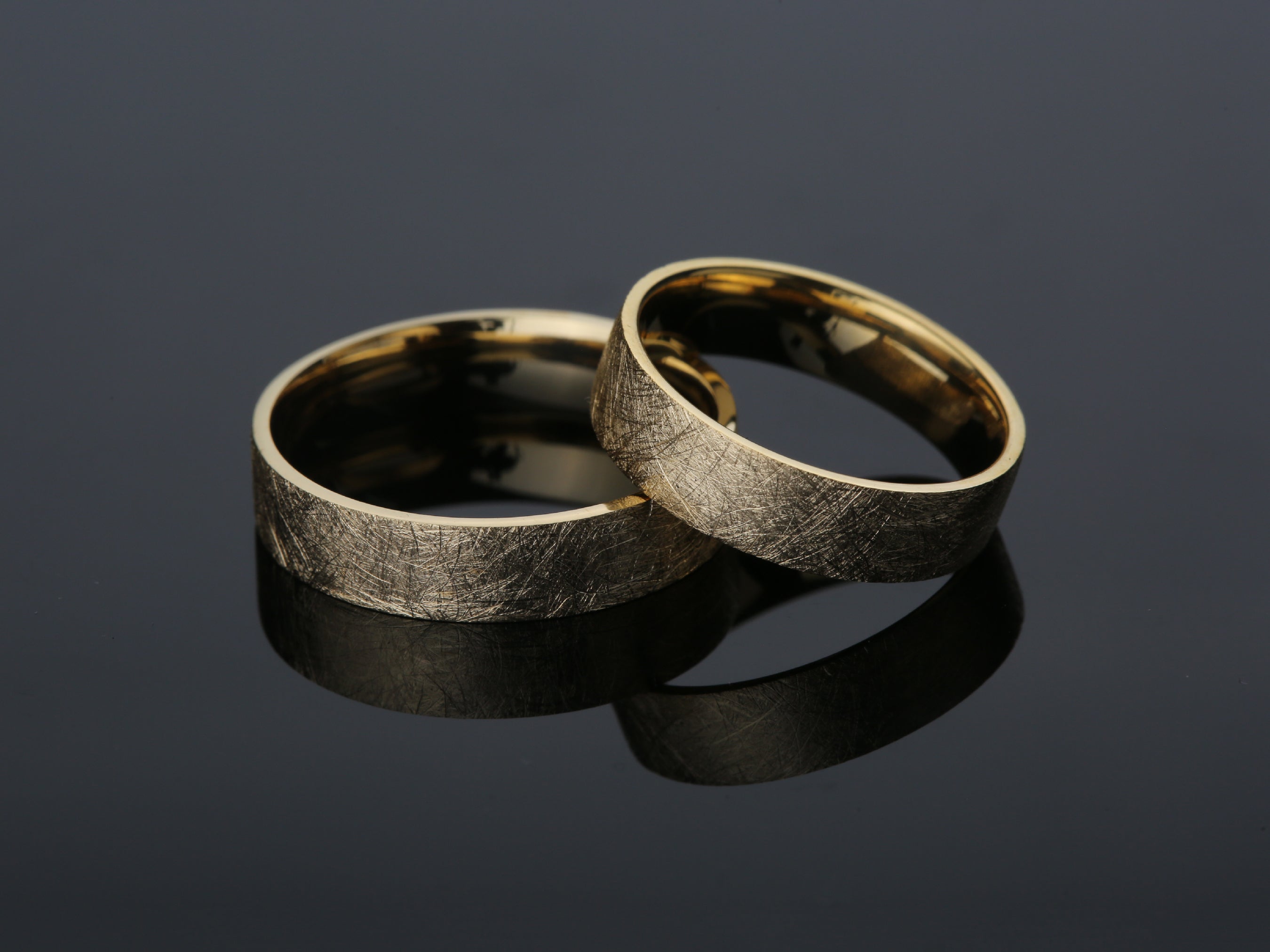 Two brushed gold wedding rings on a dark reflective surface