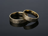 Two brushed gold wedding rings on a dark reflective surface