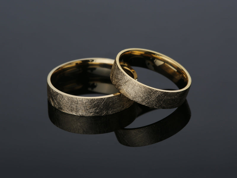 Two brushed gold wedding rings on a dark reflective surface