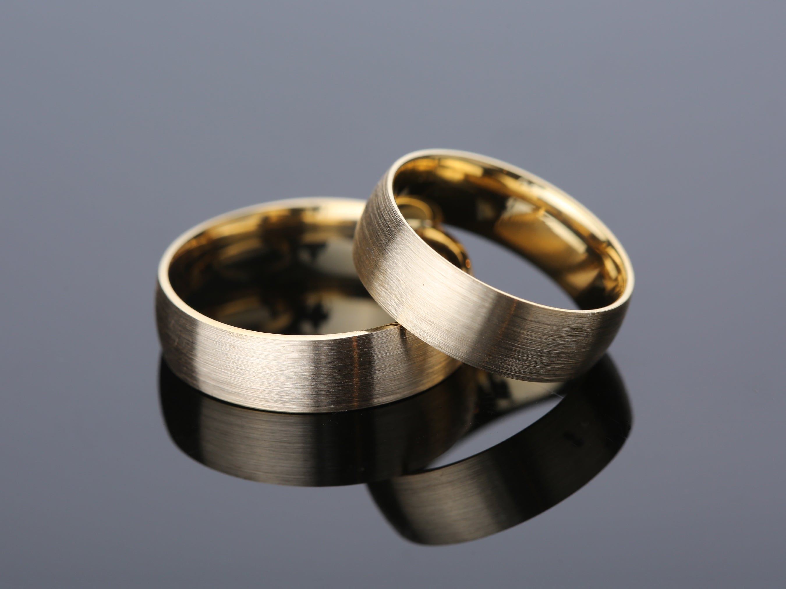 Two brushed gold wedding rings on a reflective surface
