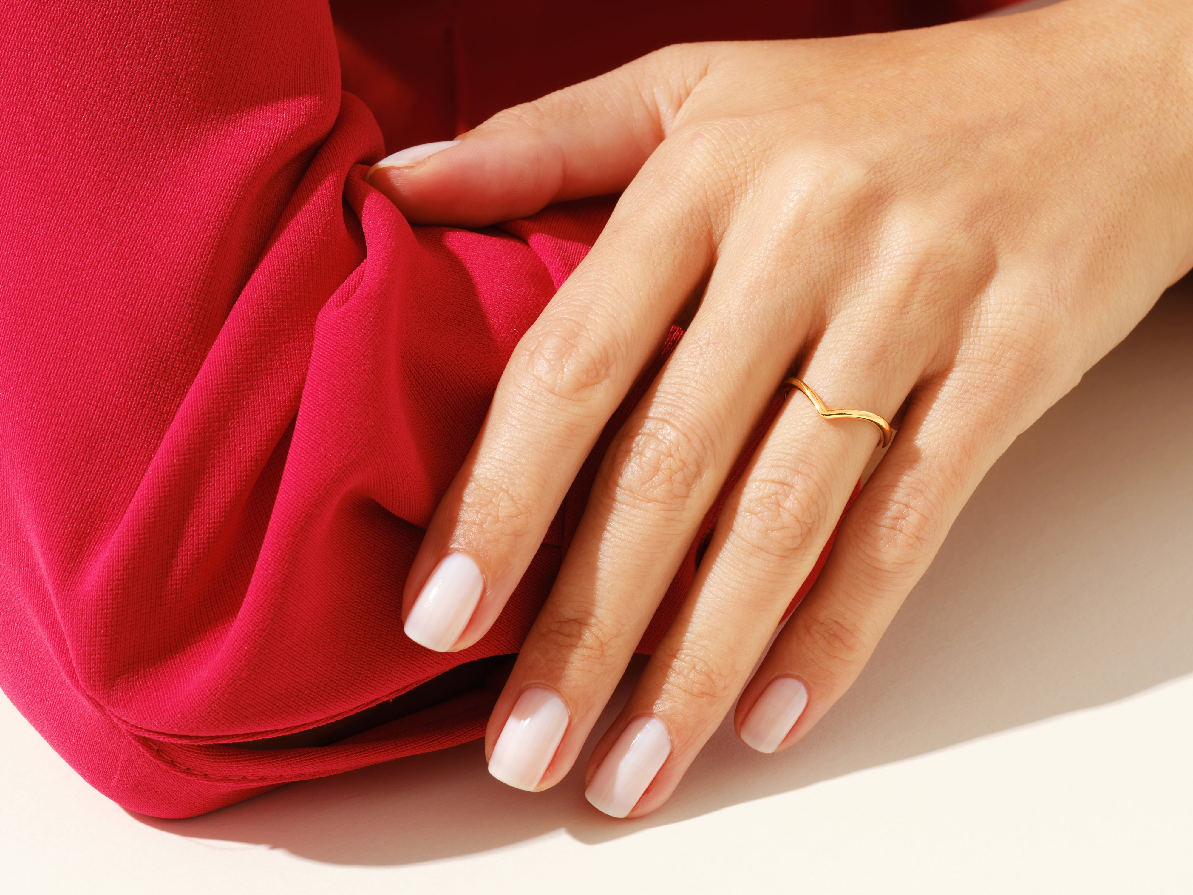 Gold chevron ring on hand with manicured nails against red fabric