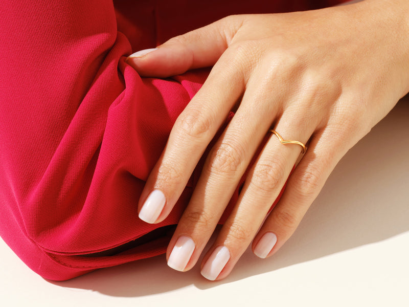 Gold chevron ring on hand with manicured nails against red fabric