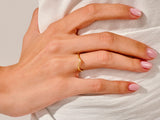 Gold V-shaped ring on a woman's hand with pink nails
