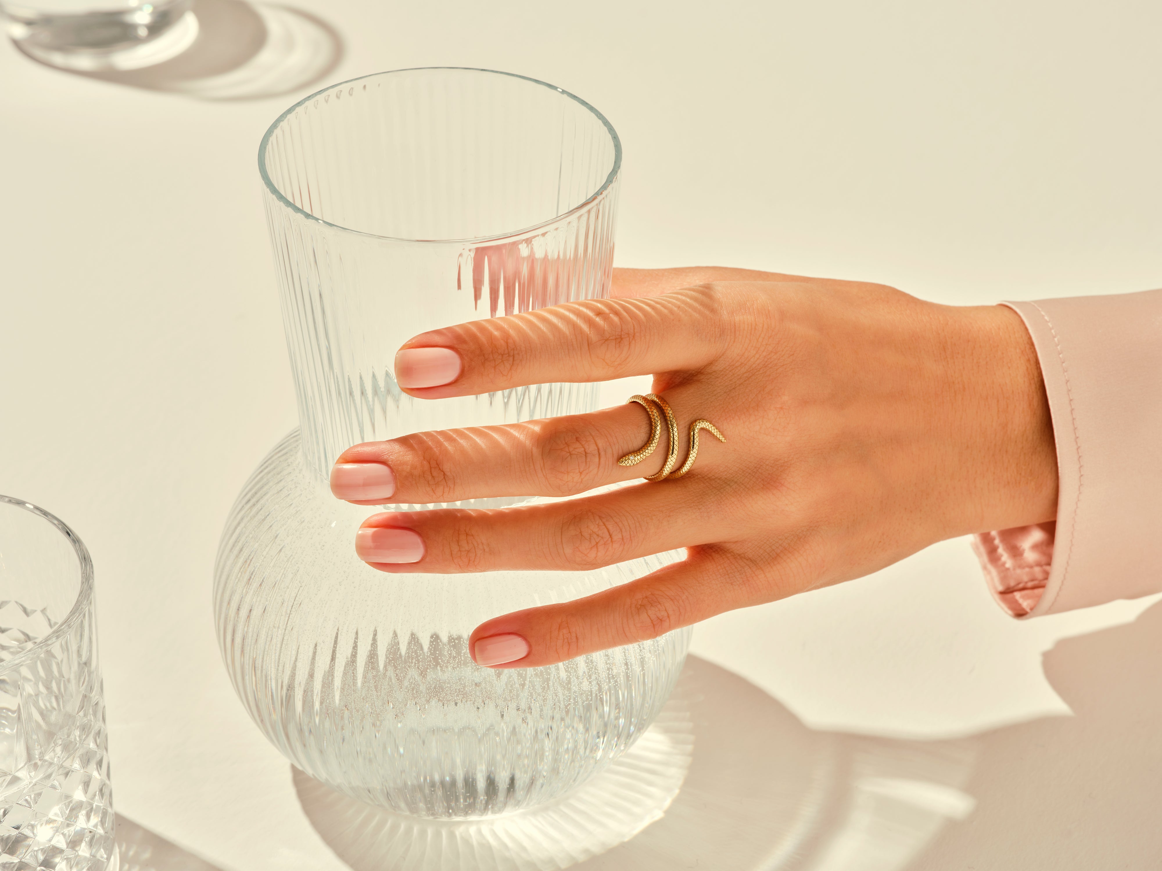 Gold snake ring on hand near elegant glassware