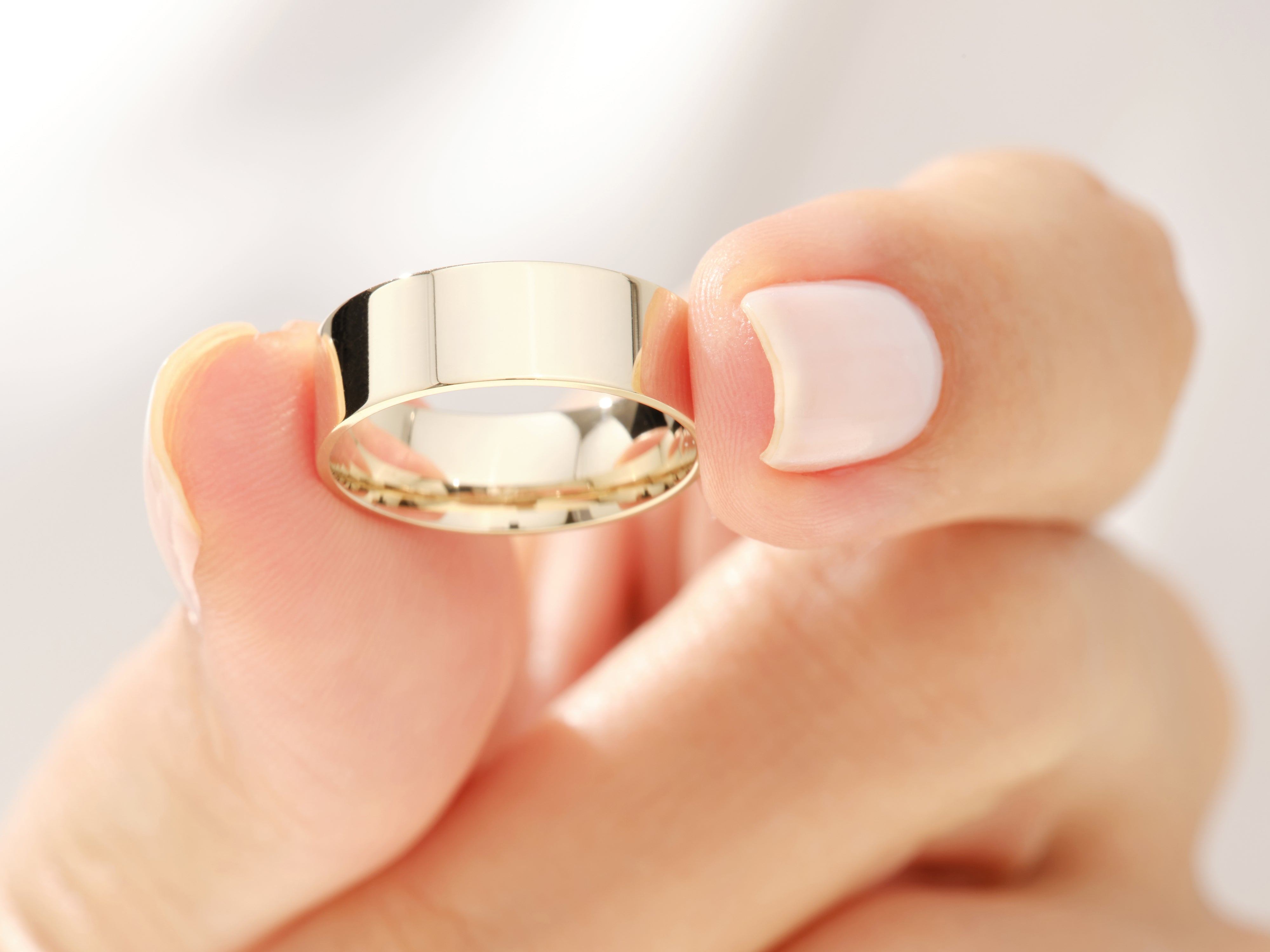 Gold band ring held by a manicured hand, jewelry product