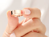 Rose gold wedding band held by manicured fingers, jewelry photography