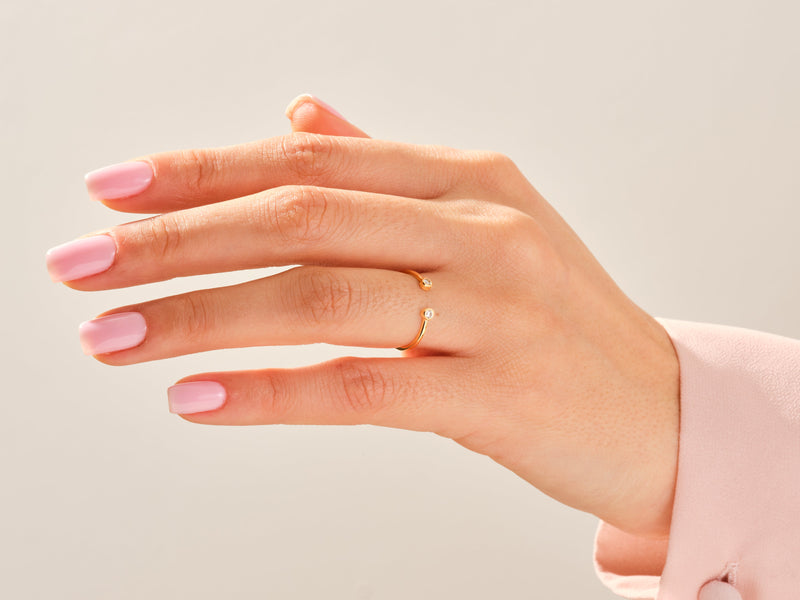 Gold diamond bypass ring on a hand with pink nails