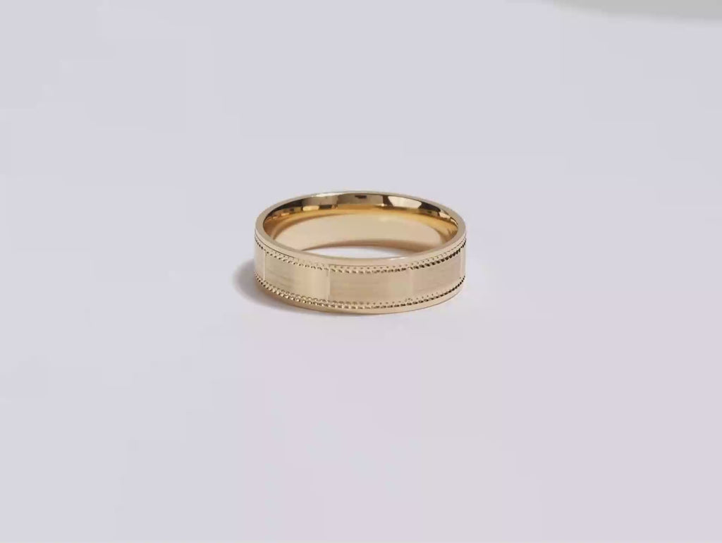 A video showing a yellow gold 6mm matte and milgrain accented men's gold wedding band spinning on a white background.