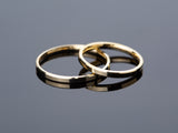 Two gold wedding bands on a reflective surface