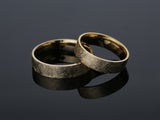 Two brushed gold wedding rings on a dark reflective surface